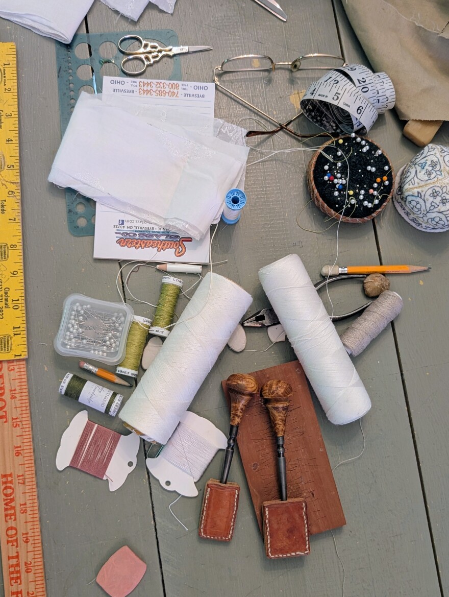 Hand sewing tools lay on a work table. 