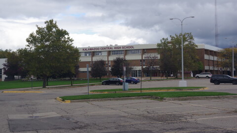 Kalamazoo Central High School is pictured on October 16, 2026. It is a red brick building with cream accents, and a large maroon sign reading "Kalamazoo Central High School" a few cars are parked in the parking lot in front of the school, and it is a grey and cloudy day. 