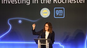 An executive gestures with her hand at a podium during a company announcement.
