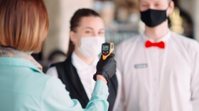 The Manager of a restaurant or hotel checks the body temperature of the staff with a thermal imaging device