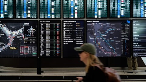 A traveler walks past screens showing outgoing and incoming flights at San Francisco International Airport ahead of the Memorial Day holiday weekend in San Francisco, Thursday, May 22, 2025.