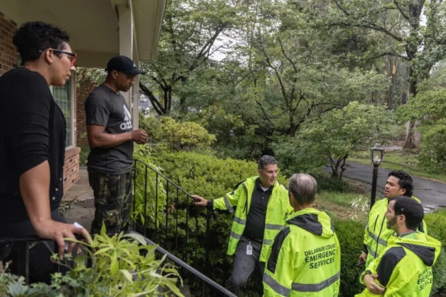 Cat and Robert Tucker stand on their porch and speak with emergency service workers in yellow coats.