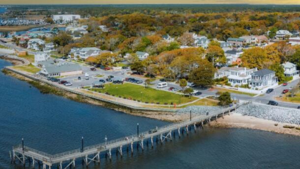 Aerial view of the City of Southport, North Carolina. A long pier extends into the ocean, the sun sets behind the city.