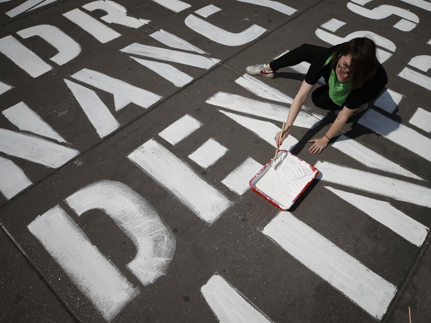A woman helps paint the names of some of more than 3,000 victims of femicide on the plaza of the Zocalo in Mexico City, on International Women's Day, Sunday. Protests against gender violence in Mexico have intensified in recent years amid an increase in killings of women and girls.