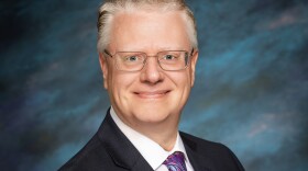 a man wearing glasses in a suit and tie smiling for a portrait