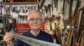 Man in glasses holding saw.