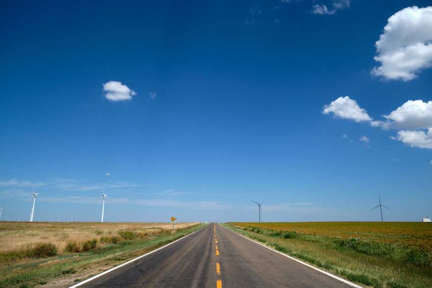 A rural highway flanked by wind turbines.