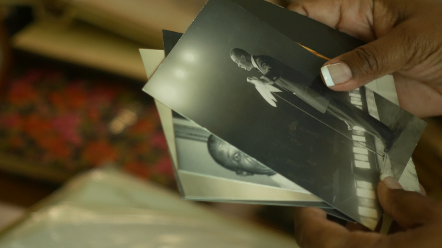 woman holds photos of Louis Armstrong in her hand.