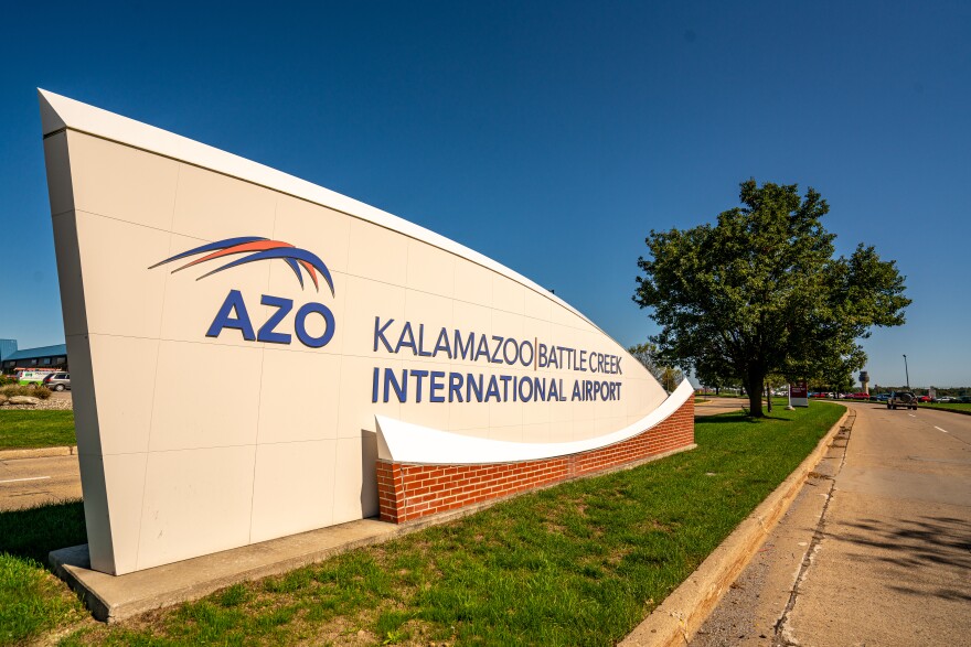 Close up view of the sign at the public entrance to the airport, which has the airport's name and code, and a long, curved shape a bit like a wing