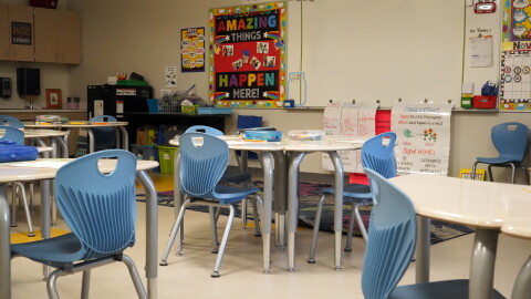 An empty classroom with round desks and blue plastic chairs around them