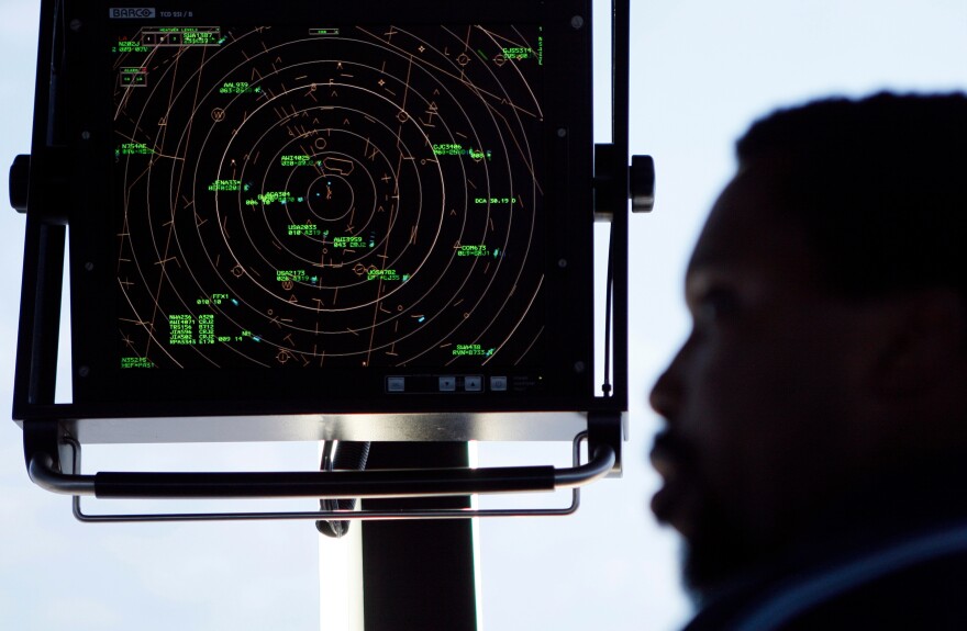 The silhouette of a man's face is seen looking towards a black screen monitor with a green bullseye on it. In green, coordinates representing planes can be seen on the screen.