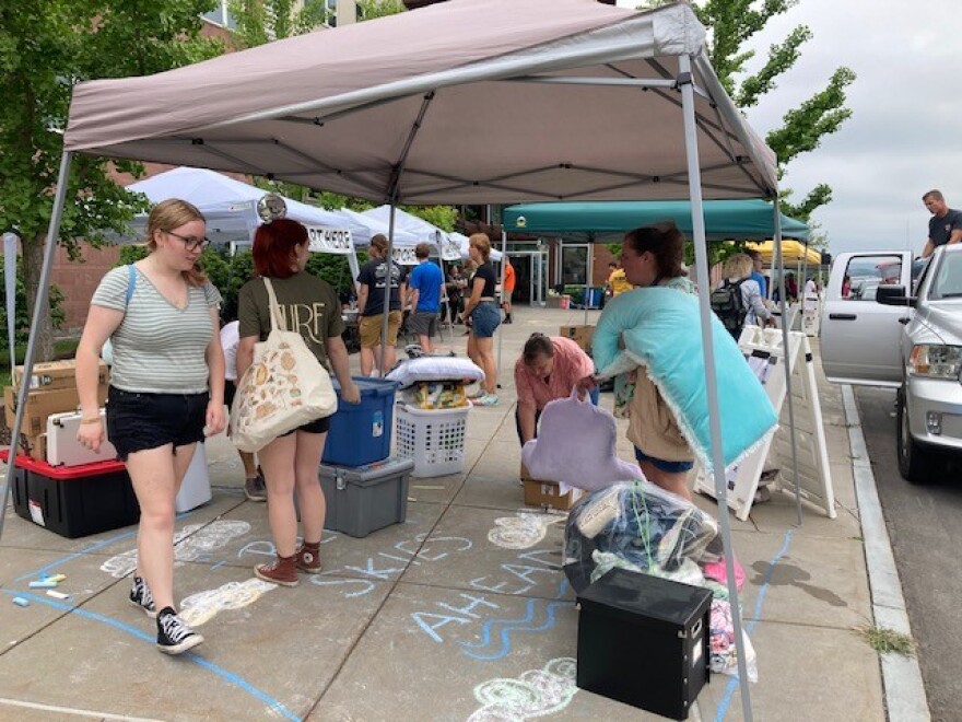 College students gather under a tent as they gather their items to move into a residence hall.