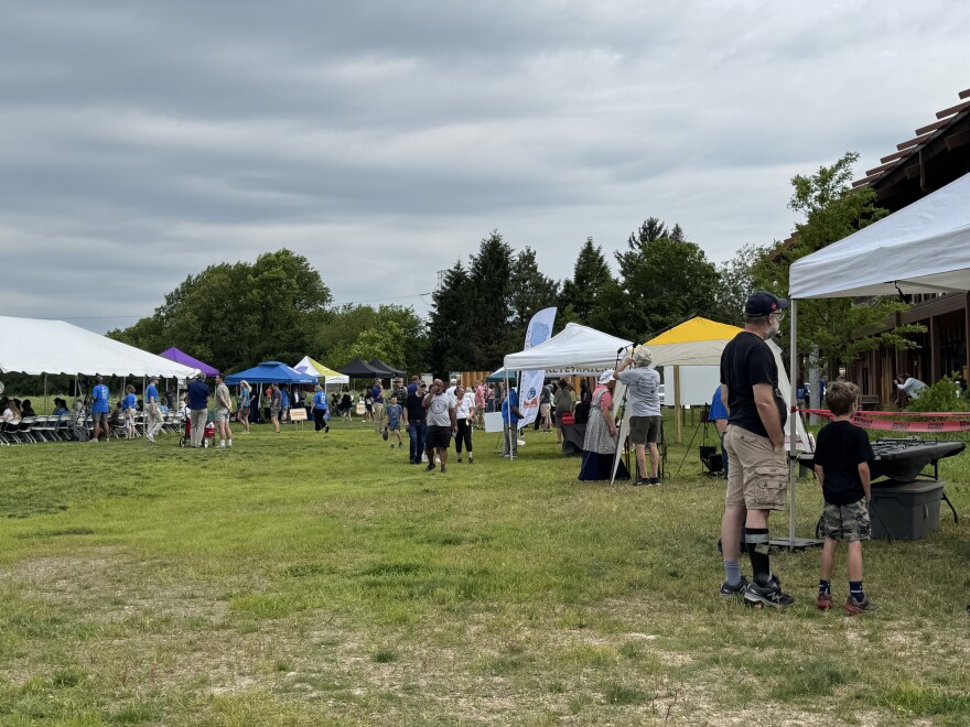 Several event tents are on a grassy field and people stand in front and under them.