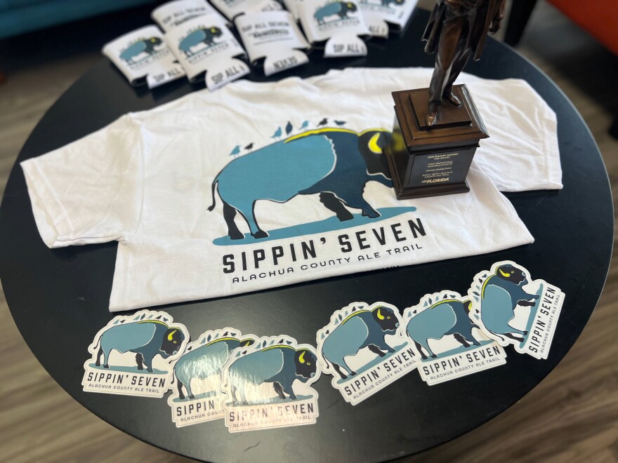 “Sippin’ Seven Alachua County Ale Trail” merchandise is available at the Visit Gainesville office. The merchandise left includes beer koozies, stickers and a T-shirt on Sept. 10, 2024. (Delia Rose Sauer/WUFT News)