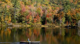 A fly fisherman paddles on a pond as fall foliage begins to show color in Campton, N.H., Sunday, Oct. 6, 2024. (AP Photo/Caleb Jones)