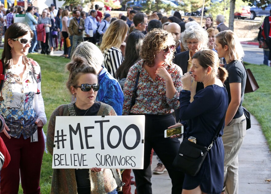 women holds up a sign that reads #metoo in front of a line of people.