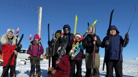 A group of children bundling up for winter weather, pose with their ski equipment and ski instructor.