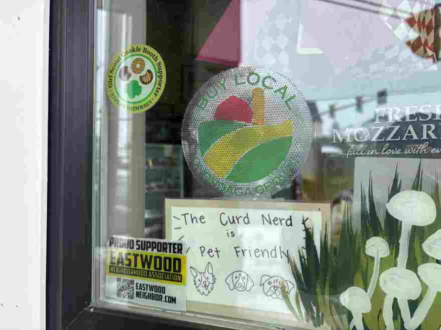Store Front window of teh Curd Nerd cheese shop in Eastwood, NY,  with signs buy local and the Curd Nerd is pet friendly.