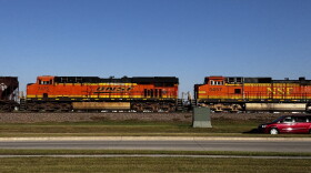 Two orange train cars with the BNSF and NSF logos ride along the train tracks on the side of a road.