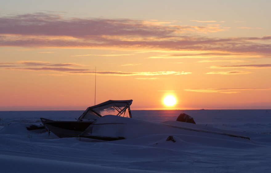 Boats buried in snow toward the edge of the lagoon at sunrise.