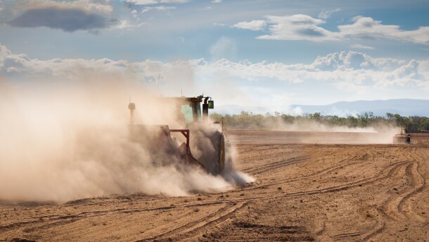 A tractor is plowing very dry and dusty farm land in a drought