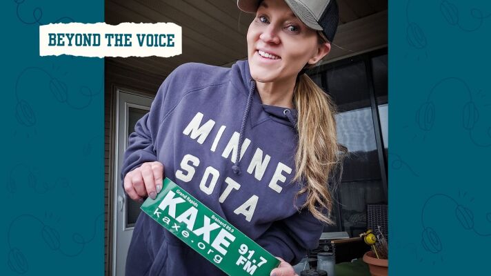A smiling woman holds a KAXE bumper sticker