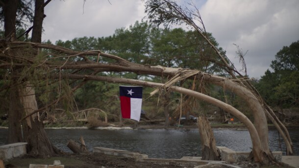 A Texas flag hangs from a flood-damaged tree on the bank of the Guadalupe River, Saturday, July 12, 2025, in Kerrville, Texas. 