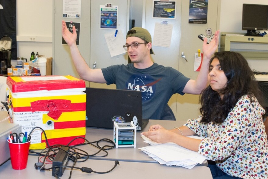 man and woman in a lab with cube-shaped satellite.