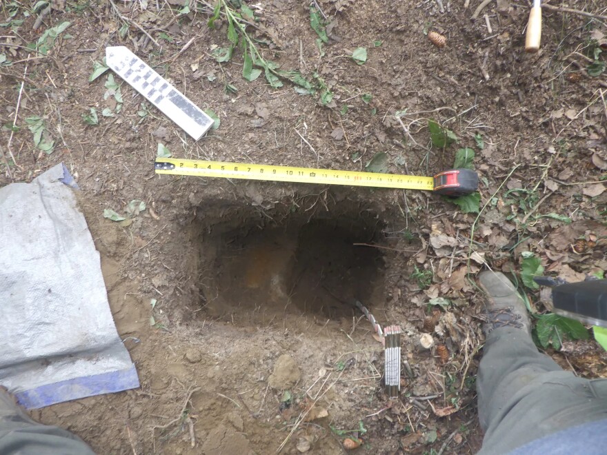 A small, rectangular hole in the ground with a tape measure across it.