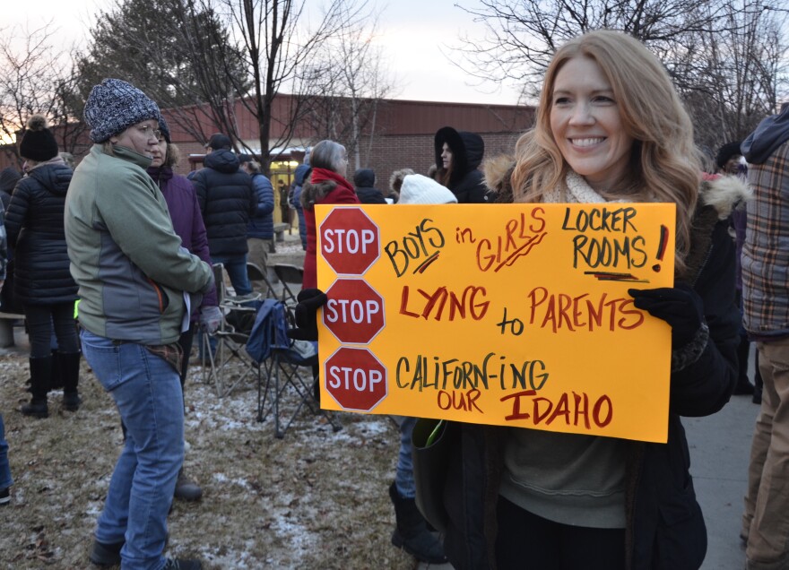 A parent standing outside of the Caldwell School Board meeting holds a neon orange sign that reads: "Stop boys in girls locker room! - Stop lying to parents - Stop California-ing our Idaho".