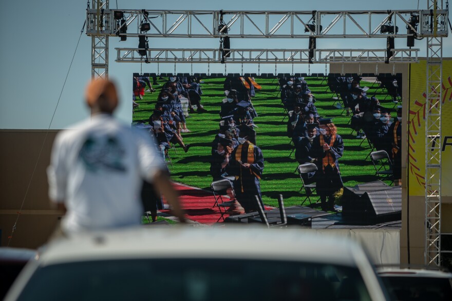 A family member watches graduation projected onto a big screen from the roof of his car. May 31, 2020.