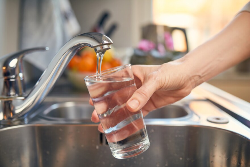 A hand fills up a clear glass of water at a sink.