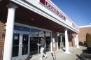 Exterior photo of the outside of a building in a strip mall. A large sign above the door reads "License Office." A person can be seen walking up to its door with some paper in their hand.