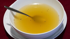 A white bowl of broth on a plate with a spoon