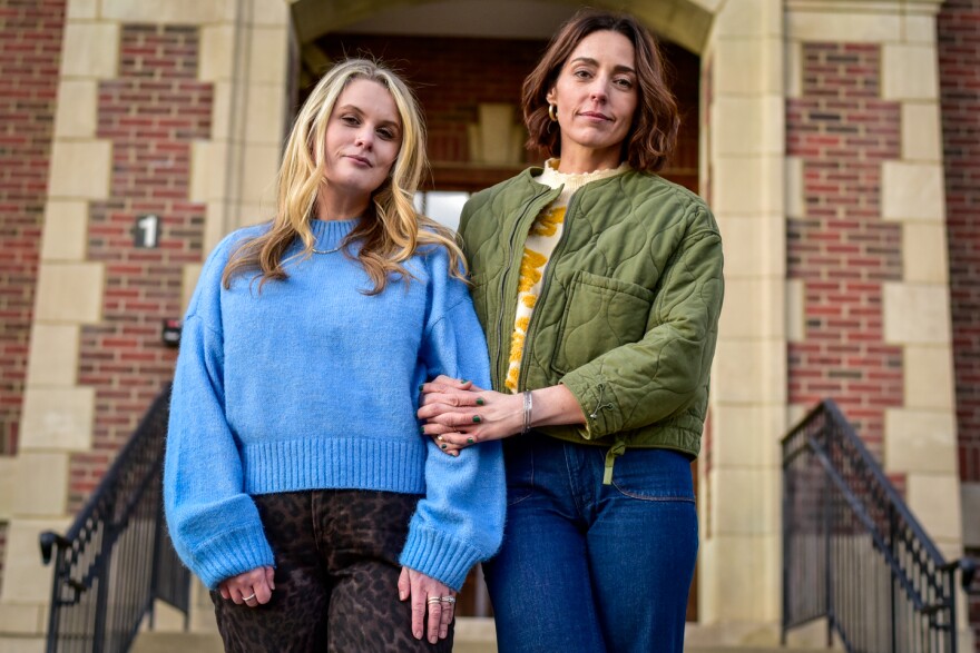 Two women pose in front of a historic brick building. 
