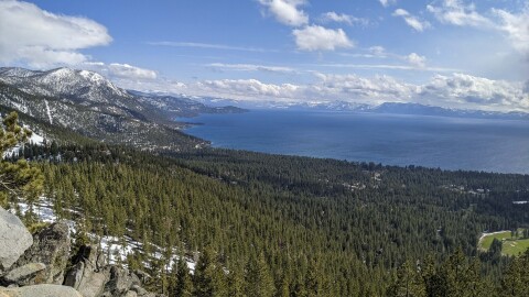 A view of Lake Tahoe with green tree covered mountains on the left and a very blue Lake Tahoe on the right. 