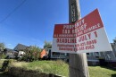 A red and white sign on a post outdoors reads "Property Tax Relief, all homeowners are eligible, deadline July 1. Behind the sign are a row of houses.