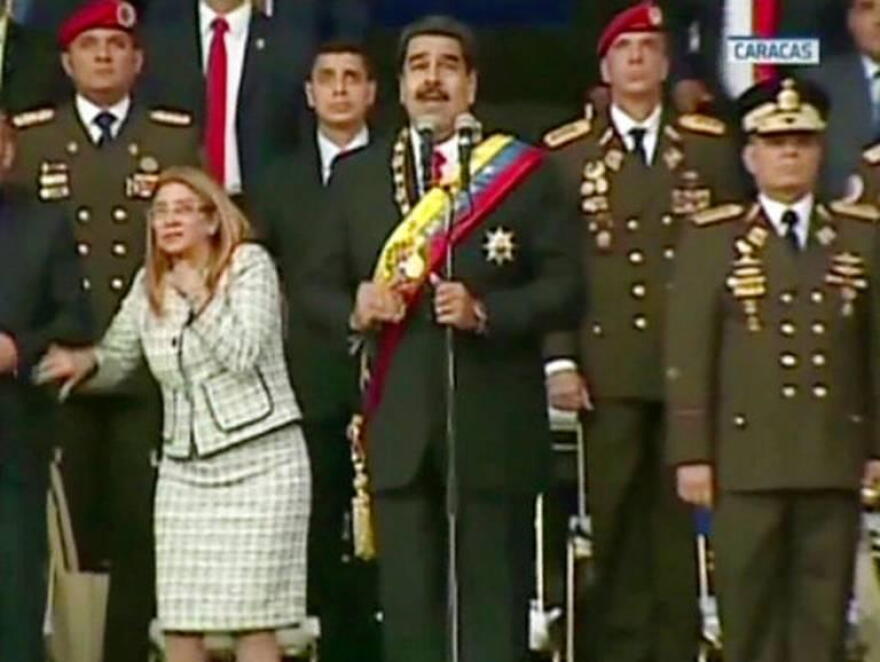 Venezuelan President Nicolas Maduro (center) watches drones explode overhead last Saturday in Caracas along with his wife Cilia Flores (left) and military guards.