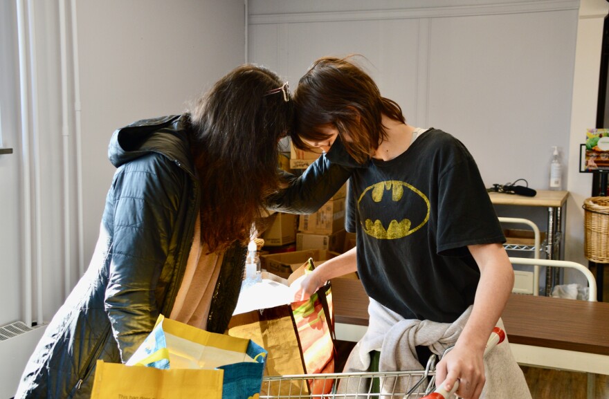 A photo of an adult and a child, wearing face masks, leaning their heads together over a grocery cart.