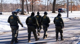 Five people in military outfits walk on an icy street.