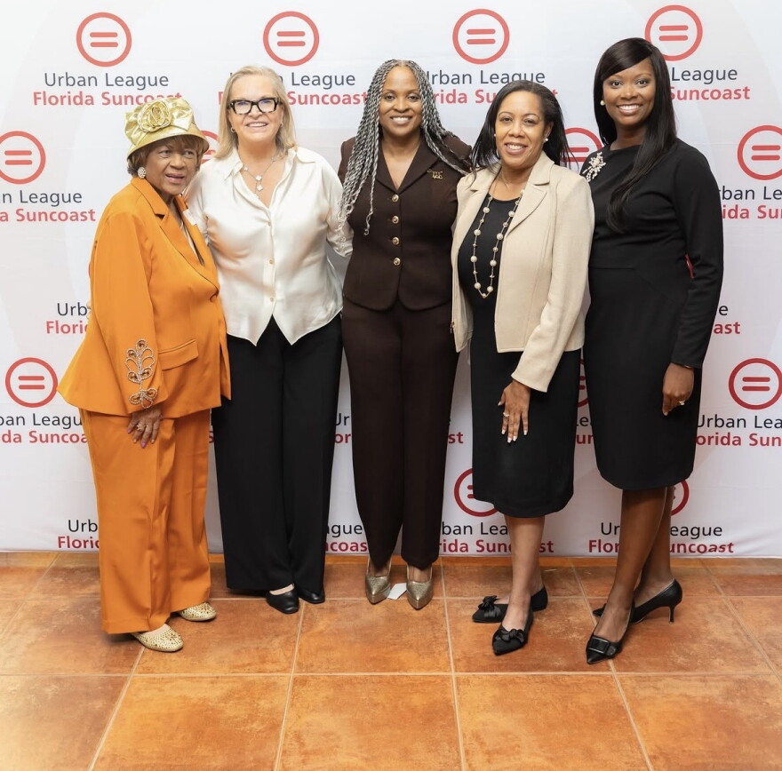 Four women standing in front of a Urban League of Florida Suncoast banner smiling 