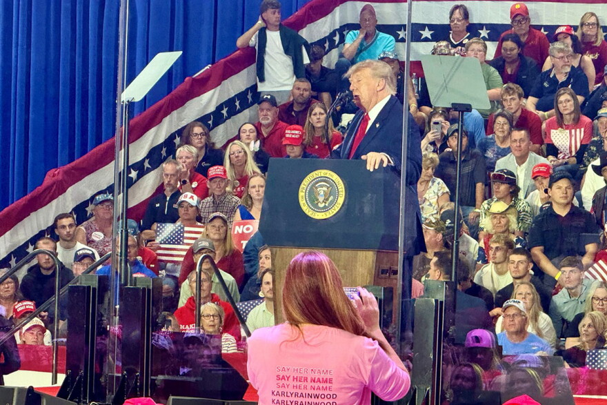 President Trump stands at a podium surrounded by a crowd.