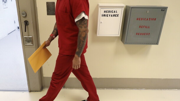 A person in an orange prison uniform walks down a hall. 
