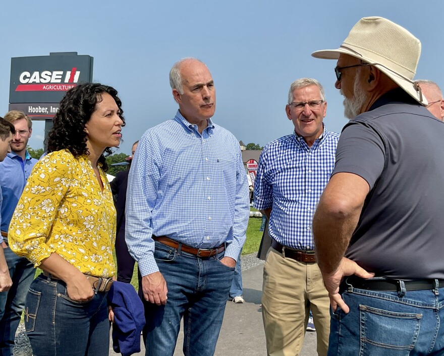U.S. Deputy Secretary of Agriculture Xochitl Torres Small, Democratic U.S. Senator Bob Casey of Pennsylvania, and Pennsylvania Secretary of Agriculture Russell Redding stand together listening to a farmer at an outside venue.