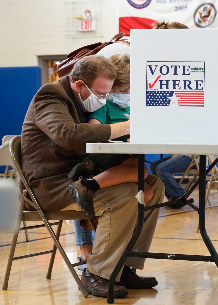 Jake Zimmerman, Democratic primary candidate for St. Louis County executive, votes while holding his 6-year-old son Gabriel at Old Bonhomme Elementary School in Olivette on Tuesday. “Are you voting for yourself, Dad?” Gabriel asked. 