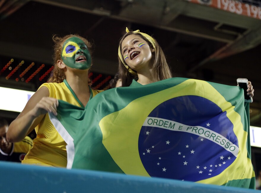 Two girls with green and yellow face paint hold a Brazilian flag
