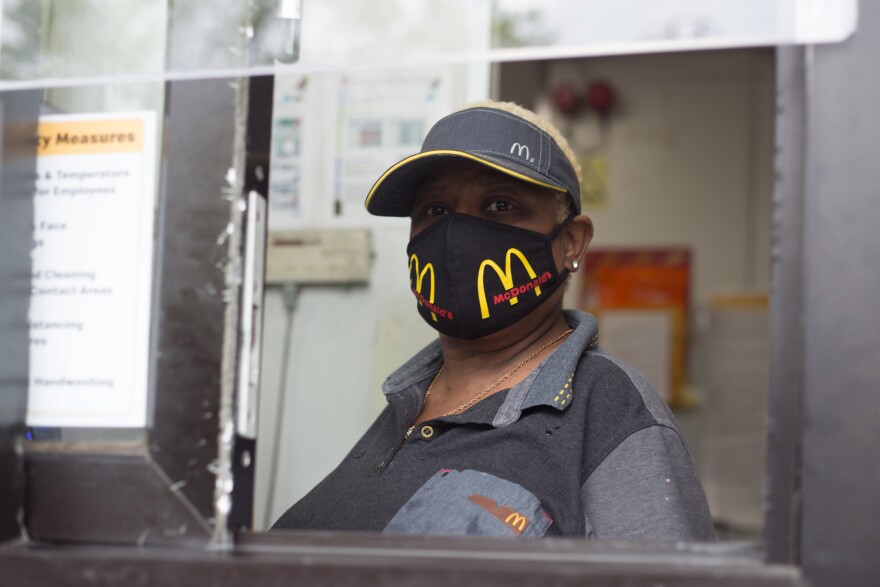 A Black McDonalds employee looks out from a drive-through window wearing a branded mask