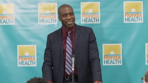 A smiling man in a dark suit against a blue Fla Dept of Health backdrop