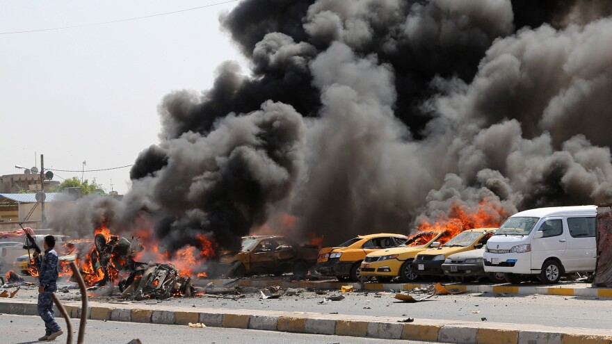 An Iraqi policeman stands near burning vehicles after a bomb hit the Shiite stronghold of Sadr City in Baghdad on May 13.