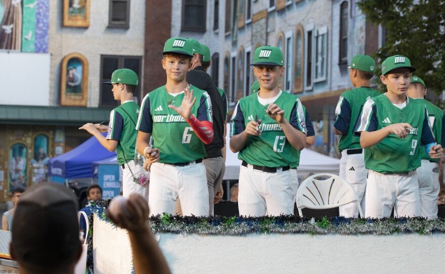 Members of the team from the Northwest region autograph baseballs during the Little League World Series parade.